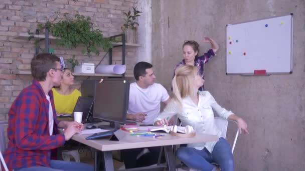 Stagiairs leren nieuwe vaardigheden aan tafel in modern kantoor luisteren naar vrouwelijke mentor in de buurt van het whiteboard en notities maken in notebooks — Stockvideo
