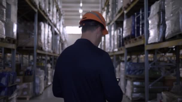 ハードハットとスーツのビジネスマンは、倉庫を歩いてタブレット上のメモを作ります — ストック動画