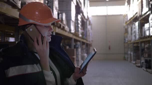 entrepôt d'usine, inspectrice en casque orange parlant sur téléphone cellulaire et utilisant une tablette 