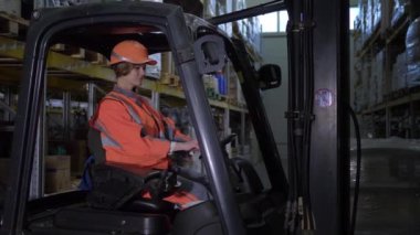sert kask ve üniforma kadın forklift kamyon sürücüsü kamera bakar ve depoda gülümsüyor
