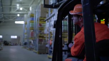 operatör, forklift kamyonundaki depoyu, mallarla birlikte raflardan geçerek denetler