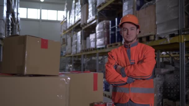 Retrato de trabajador con las manos dobladas en los soportes del pecho en uniforme naranja brillante cerca de muchas cajas en almacén — Vídeos de Stock