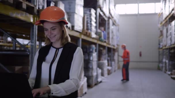 Trabajadora de almacén mujer en el uso de sombrero duro portátil y toma notas en bloc de notas — Vídeos de Stock