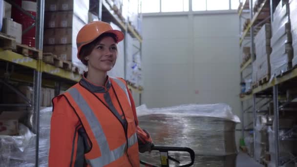 femme au travail dur, ouvrier en uniforme tirant chariot avec des boîtes entre les rangées de racks sur l'entrepôt 