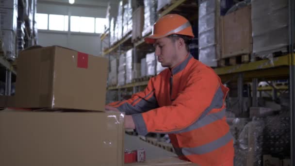 Workerman in uniform packs cardboard boxes with sticky tape in warehouse — Stock Video