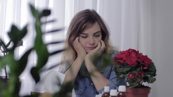 Meisje lijdt aan seizoensgebonden allergieën is voortdurend niezen en blazen neus in een zakdoek vanwege bloemen, die zijn op tafel naast medicijnen — Stockvideo