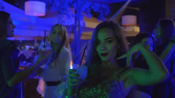 Fiesta nocturna, retrato de muy hermosa joven sexy mujer que se divierte y baila con amigos en discoteca mientras bebe un cóctel de alcohol exótico — Vídeo de stock