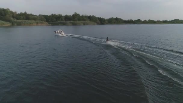 Active lifestyle, aerial view athlete surfing on wakeboard along the river behind a motor boat at evening outdoor in slow motion — Stock Video