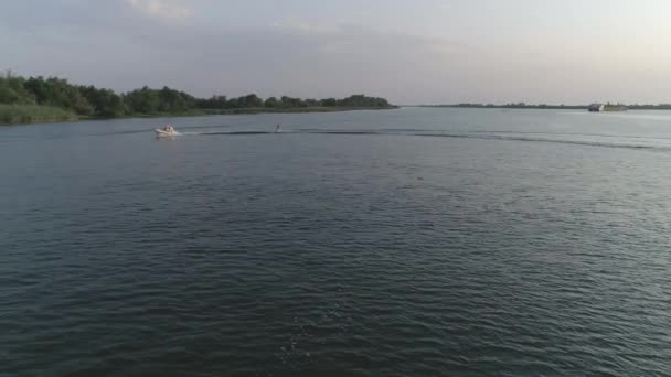 Luchtfoto van sport persoon surfen op Wakeboard achter motorboot met water spatten langs rivier in slow motion op achtergrond natuur — Stockvideo