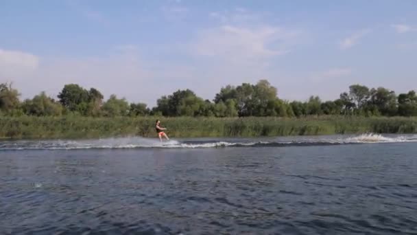 Extrém sportok, szörfös férfi lovagol a fedélzeten a motorcsónak mögött a folyón fröccsenő víz a háttérben a természet és a kék ég — Stock videók