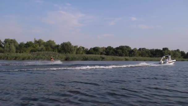 Deporte acuático extremo, el hombre surfeando en wakeboard detrás de la lancha con salpicaduras de agua a lo largo del río en el fondo de la naturaleza — Vídeo de stock