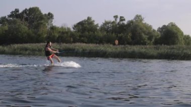 yavaş hareket sazlık arka planda nehir boyunca su sıçramaları ile motorbot arkasında gemide sportif adam wakeboarder eğitim