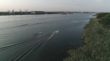 motorbot arkasında nehir boyunca wakeboard üzerinde sörfçü sürmek ve yavaş hareket, havadan görünümünde şehrin arka planda akşam ip kolu tutar