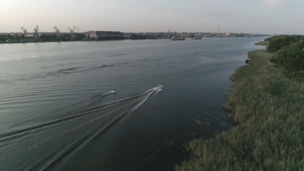 Surfista paseos en wakeboard a lo largo del río detrás de la lancha y sostiene la manija de la cuerda en la noche en el fondo de la ciudad en cámara lenta, vista aérea — Vídeos de Stock