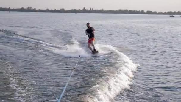 Surfing, coola Sportsman Rider ombord bakom motorbåt på floden med stänk vatten på bakgrunds natur — Stockvideo