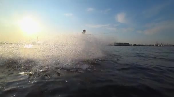 極端なライフスタイル、スポーツマンは川のモーターボートの後ろにボードに乗って、黄金の太陽と青空を背景に休暇中にカメラレンズに水をはねる — ストック動画
