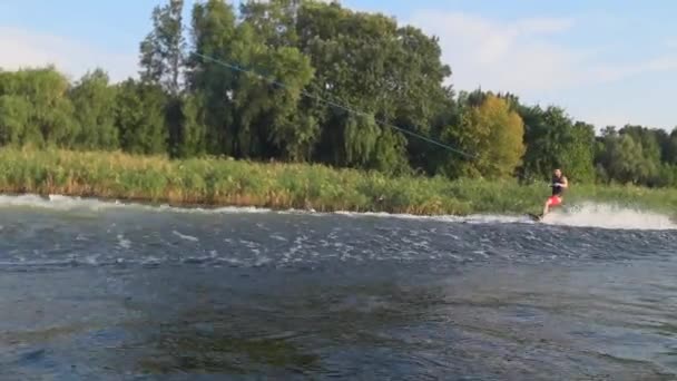 Wakeboarding, hombre atlético en los paseos por el río a bordo detrás de la lancha con salpicaduras de agua durante las vacaciones de verano — Vídeos de Stock