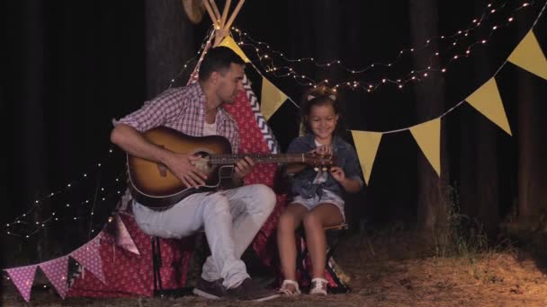 Padre e hija tocar la guitarra y llamar a mamá en picnic familiar durante el fin de semana al aire libre en fondo wigwam — Vídeos de Stock