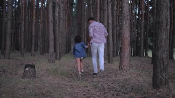 Alegre papá con hija cogida de la mano corriendo entre filas de pinos en el bosque durante el fin de semana por la noche en cámara lenta — Vídeos de Stock