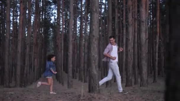 Repos en famille dans la forêt, jeune papa s'amuser et jouer à rattraper avec fille mignonne entre rangées de pins à l'extérieur au ralenti — Video