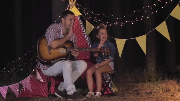 Picknick 's nachts, vader en dochter bellen mam met eten bij de picknick tijdens het diner op vakantie in het bos tegen de achtergrond van wigwam — Stockvideo