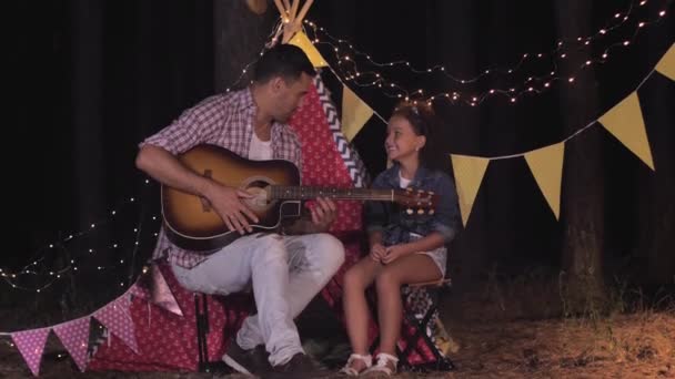 příbuzní, milující otec hraje na kytaru se svým dítětem během pikniku v lese o letním víkendu