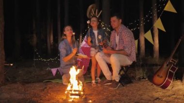 Aile atmosferi, kızlarıyla komik ebeveynler tehlikede olan marşmelovları kızartıyorlar, gece pikniği sırasında ormanda gülüyorlar.