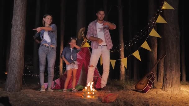 Família amorosa, mãe pai e filha rir alegremente dançar em torno de fogo na floresta durante a noite piquenique em férias na floresta — Vídeo de Stock