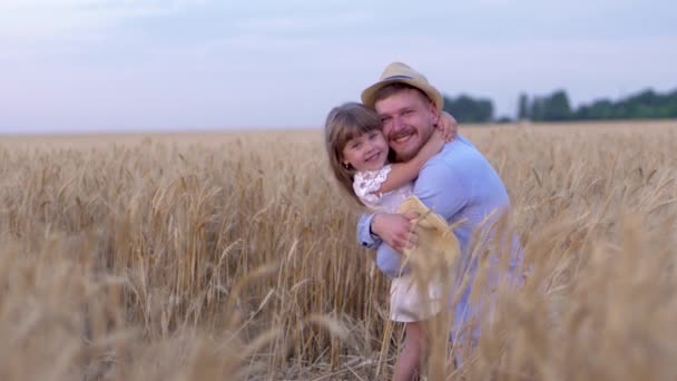 Relacje rodzinne, szczęśliwy mężczyzna radośnie przytula małą radosną dziewczynkę i uśmiecha się na polu z dojrzałą pszenicą podczas dojrzałych zbiorów — Wideo stockowe