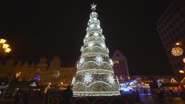 Beautiful Christmas tree with colorful toys and glittering garlands, people are walking on Market Square during the holidays at evening — Stock Video