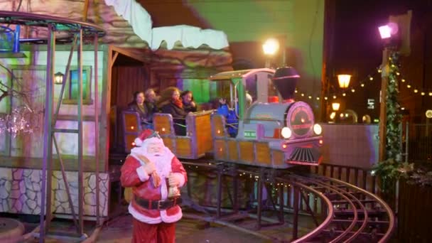 Szórakozás a karácsonyi vásár, boldog emberek lovagolni megvilágított attrakció vonat sínen — Stock videók