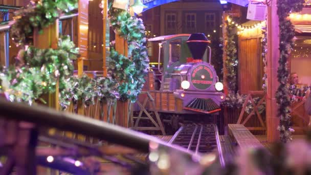 Train with wooden wagons rides on rails on background of christmas lights and decoration at evening — Stock Video