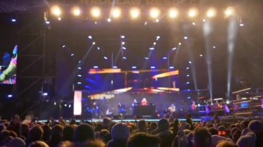 konser açık havada, insanlar akşam duman özel efektler ve spot ışıkları ile arka plan sahnesine karşı uyum içinde ellerini kaldırın