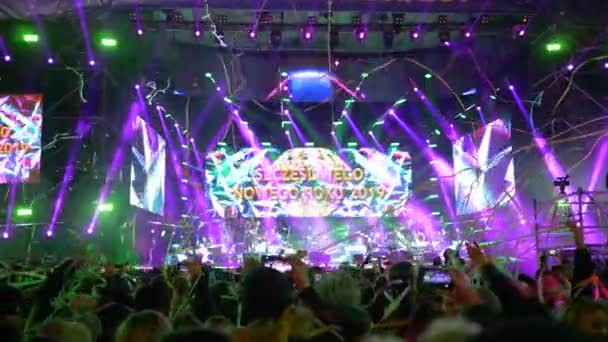 Confeti de colores festivos cayendo sobre multitud de personas filman el video en el teléfono del escenario de concierto con pantalla grande que frase escrita Feliz Año Nuevo 2019 — Vídeos de Stock