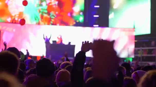 Человек в толпе людей с мобильным телефоном в руках снимает сцену концерта в ярких огнях вечером — стоковое видео