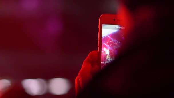 Κινητό τηλέφωνο στα χέρια ενός αγνώριτου προσώπου πυροβολεί μια σκηνή συναυλία στα φώτα σε ένα πλήθος ανθρώπων το βράδυ — Αρχείο Βίντεο