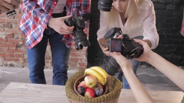 Активні фотографи на майстер-класі фотографують фрукти в кошику на дерев'яному столі, використовуючи камери і мобільний телефон, крупним планом — стокове відео