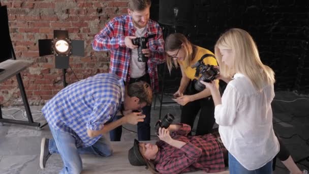 Backstage van fotoshoot, jonge fotografen met professionele apparatuur Foto's maken gelukkig meisje in hoed die op tafel met camera ligt — Stockvideo