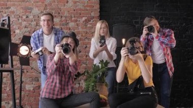 elinde farklı dijital kameralar ile gülümseyen genç fotoğrafçılar stüdyo yakın masterclass sırasında bir tuğla duvar ve lambalar arka plan üzerinde fotoğraf çekmek