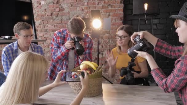 Master class com equipamentos em estúdio, jovens fotógrafos aprendem a tirar fotos de frutas em cesta com câmeras de uso e telefone celular — Vídeo de Stock