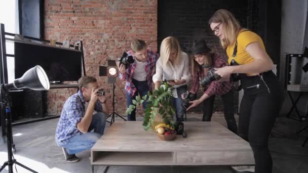 Fotógrafos con cámaras y teléfono móvil durante la clase magistral toman fotos de naturaleza muerta en el fondo de softboxes y pared de ladrillo — Vídeos de Stock