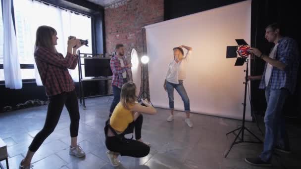Fotógrafos na moda com assistentes tirar fotos com câmeras DSLR com modelo bonito durante oficina de fotos no fundo de lâmpadas de iluminação — Vídeo de Stock