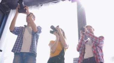 İşteki fotoğrafçılar, ellerinde dijital kameralar olan genç ve güzel insanlar stüdyoda fotoğraf çekiyorlar ve çekimleri tartışıyorlar.