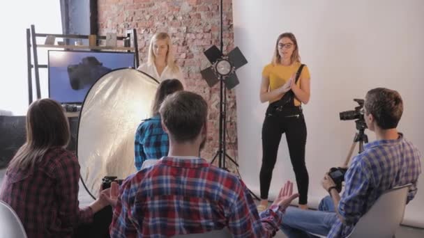 Equipo fotográfico, un fotógrafo profesional con un asistente enseña a trabajar con reflector en el taller para fotógrafos en el estudio — Vídeos de Stock