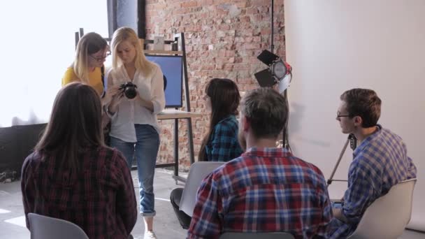 Fotoschool, jonge professionele leraar fotograaf vertelt instellingen van Dslr camera voor beginners fotografen op de achtergrond van TV met foto van apparatuur — Stockvideo