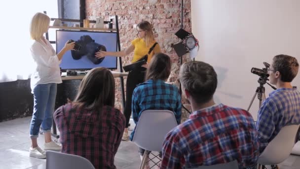 Workshop av fotografer, profesjonelle kameramenn underviser unge stilistiske personer - grunnleggende personer innen fotografi i studio på bakgrunn av TV med bilde av utstyr – stockvideo