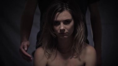 Aile içi şiddet sorunları, arka plandaki adam kadın kurbana ağzını kapatıyor ve elini yüzüne koyuyor, çaresiz kadın duygusal çöküntüde kameraya yardım çağrısı yapıyor.