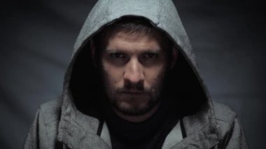 Korkunç adam portresi, kapüşonlu kötü bir erkek portresi. Karanlık arka planda zalim bir bakışla kameraya bakıyor. Şiddet kavramı.