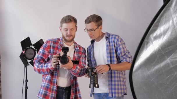 Молоді творчі фотографи обговорюють фотографію під час модної майстерні в студії на фоні освітлювальних ламп — стокове відео