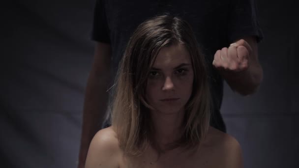Сльозна дівчина проти домашнього насильства махає головою з написом на руці Ні на тлі жорстокого чоловіка, що показує кулак в чорній кімнаті — стокове відео